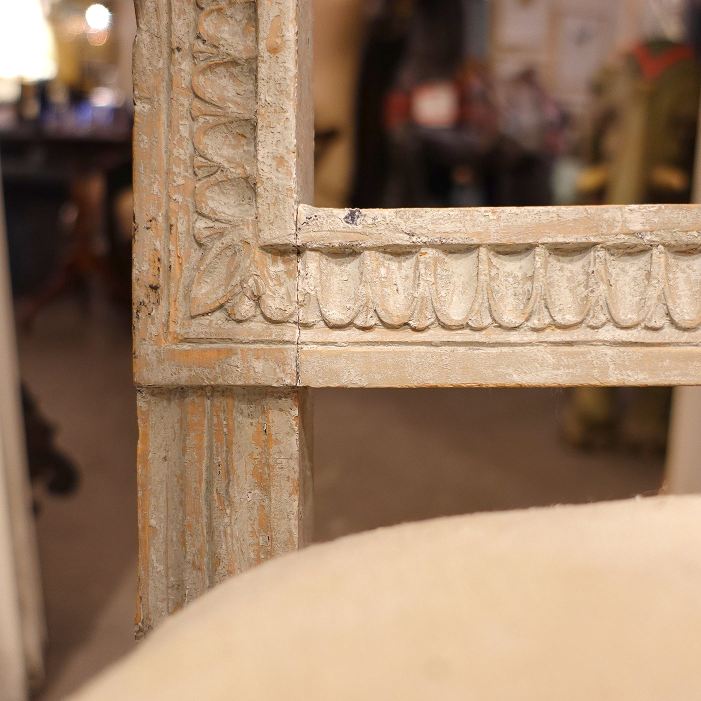 Close-up detail of an Antique Swedish Gustavian hand-carved time worn accent chair in neutral tones with a linen cushion.