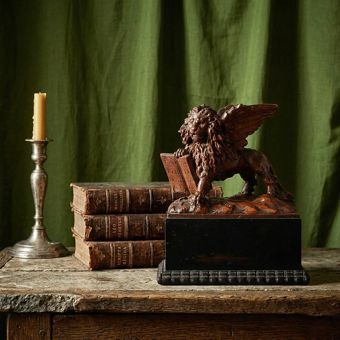 Decorative winged lion figure on a pedestal with books and a candlestick against a green curtain background.