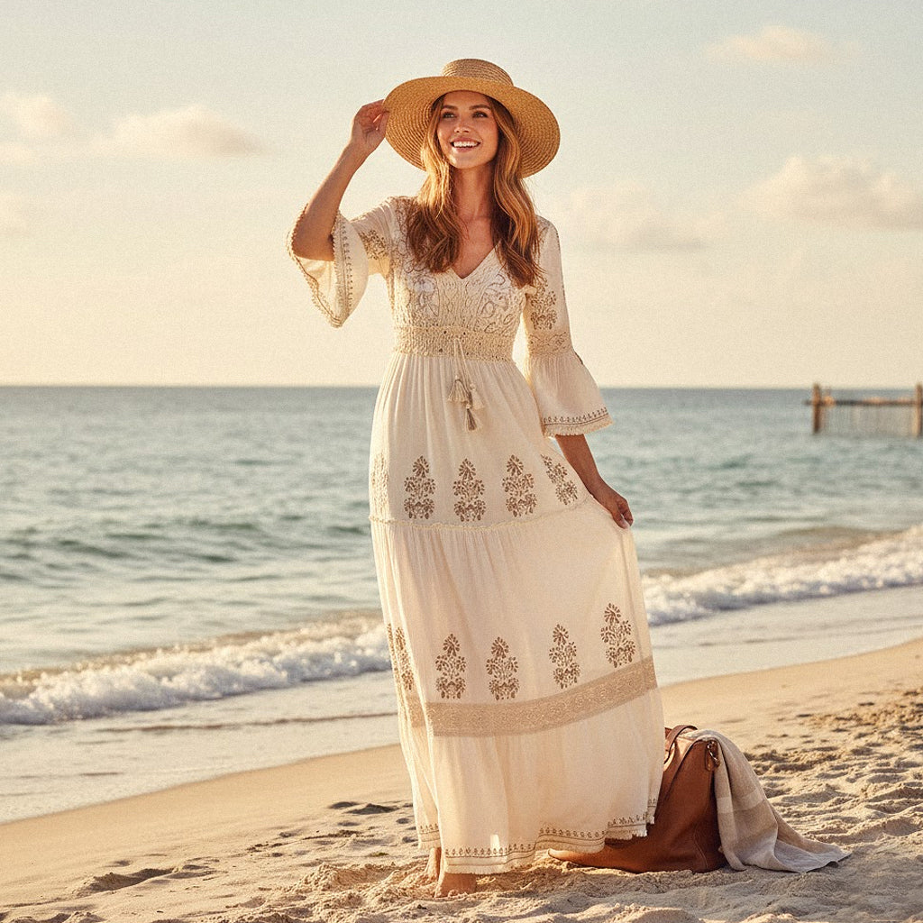A smiling model wearing a bohemian floral maxi dress with lace trim and embroidery on a sun-drenched beach, embodying a romantic, high-end preppy summer aesthetic.