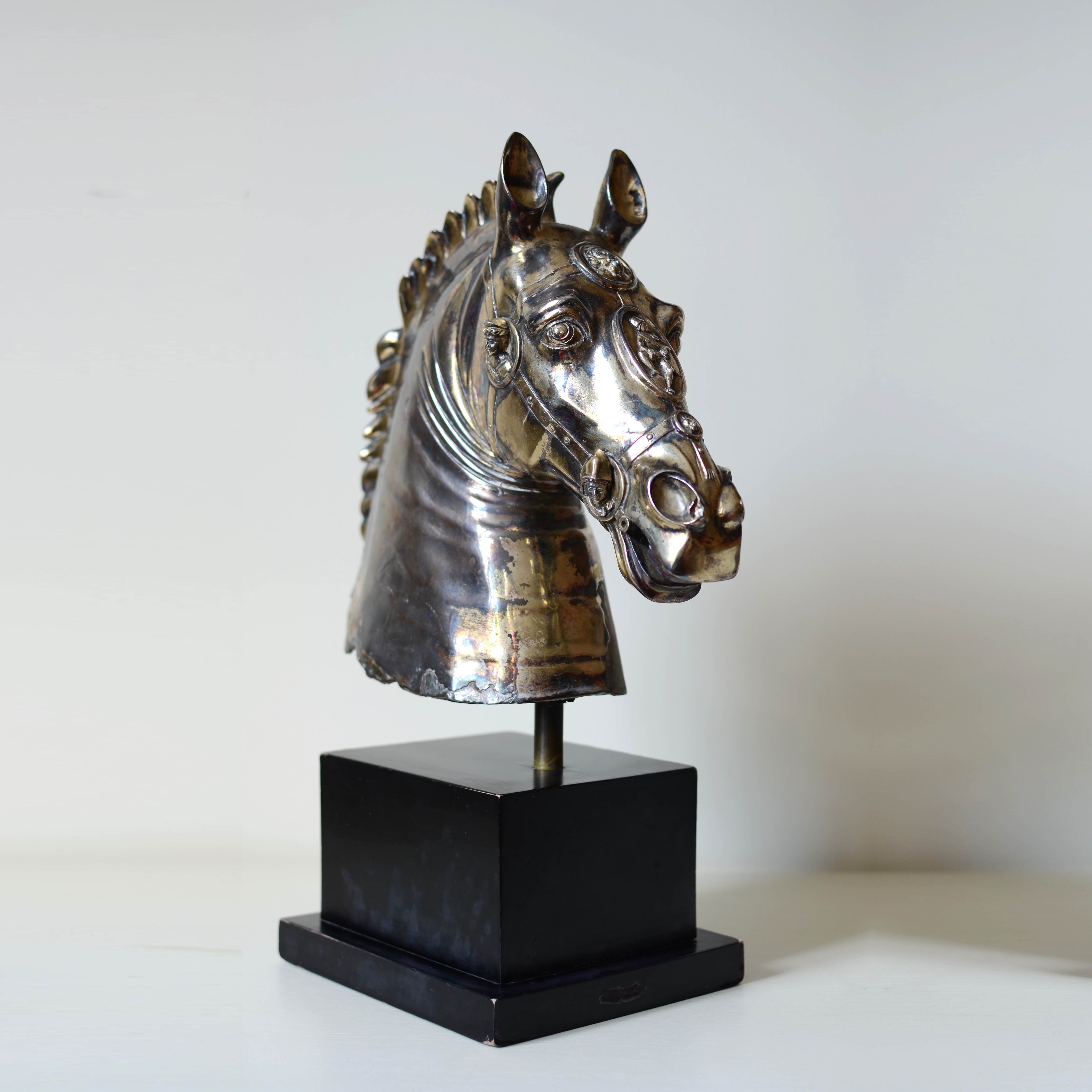 Metallic horse head sculpture on a black base against a white background
