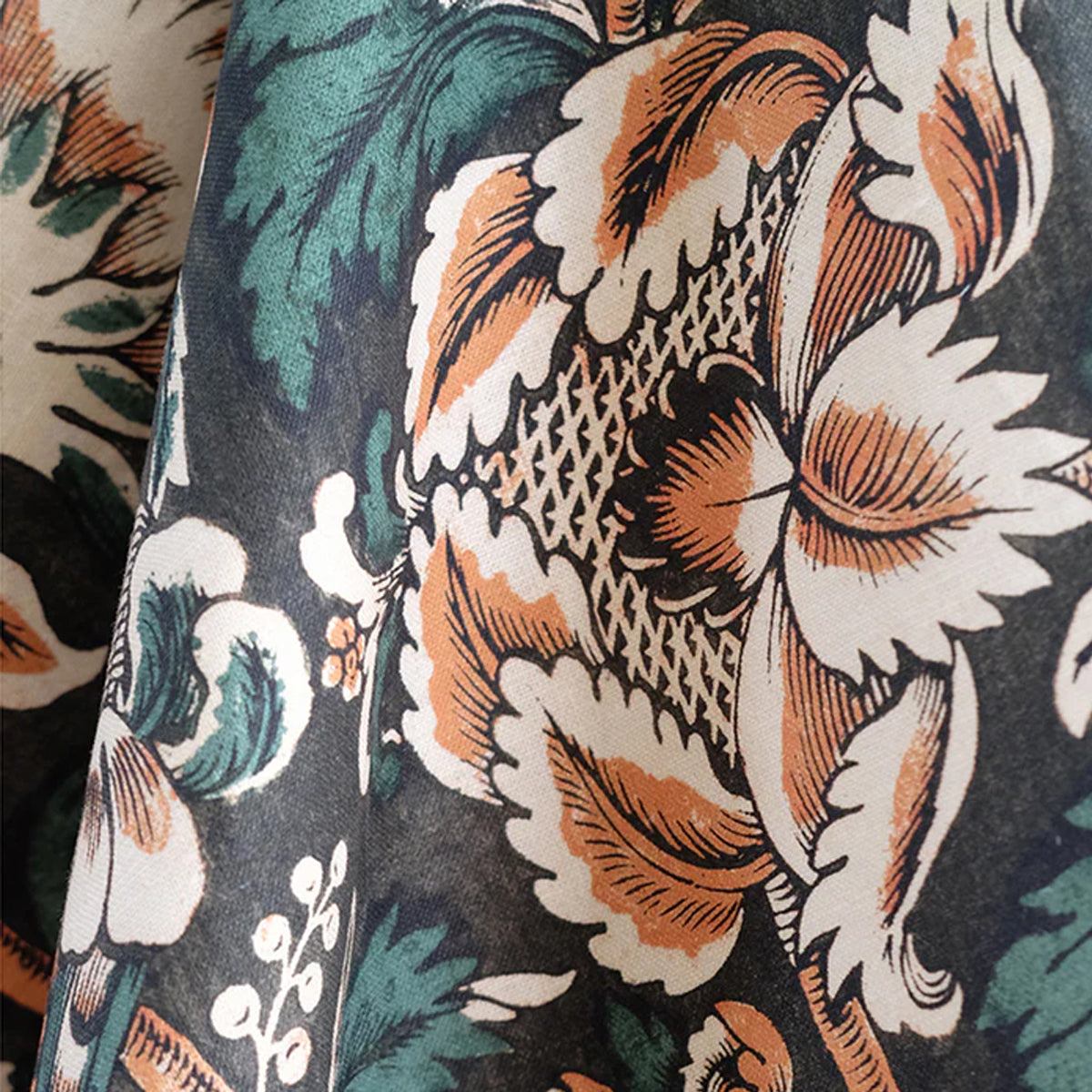 Close-up of a floral fabric with orange, green, and white flowers on a dark background.