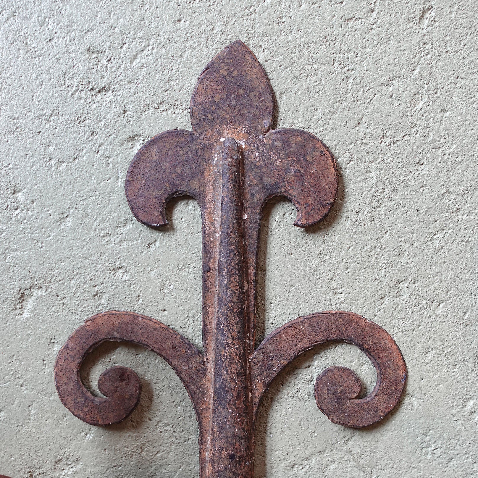 Rustic iron fleur-de-lis design on a textured wall.