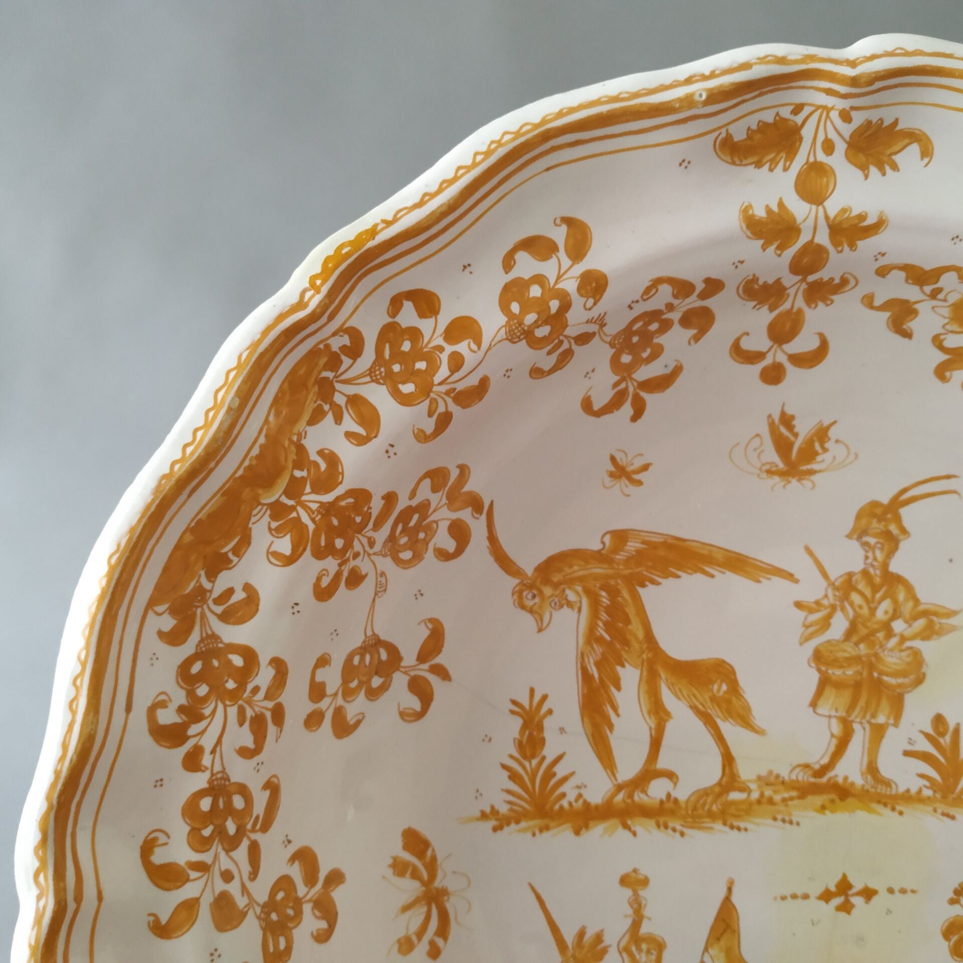 Detail of a rare 18th-century French Moustiers Faience earthenware deep plate featuring yellow monochrome ochre grotesque decoration in the style of Jacques Callot, curated by Le Historique.
