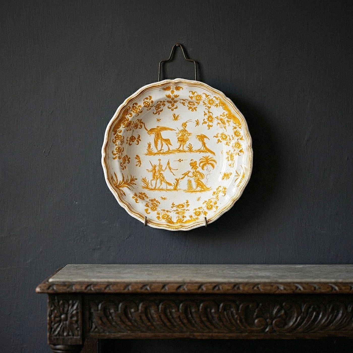 Decorative plate with gold designs on a dark wall above a wooden shelf.