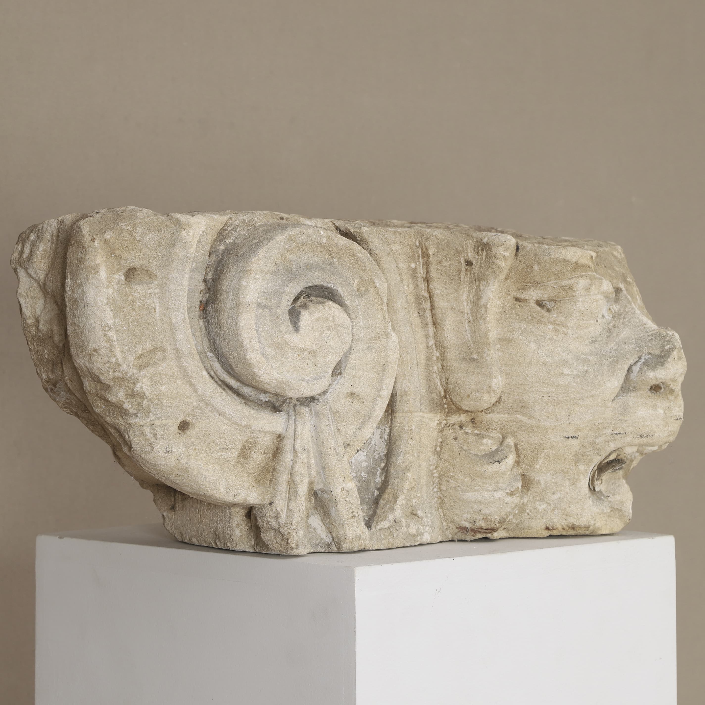 A curated, weathered European antique modillion, c. 16th-century. Carved from high-quality Caen stone, showing a detailed Greco-Roman Ionic scroll and a mannerist chimera face. Provenance from the Sennegon collection.
