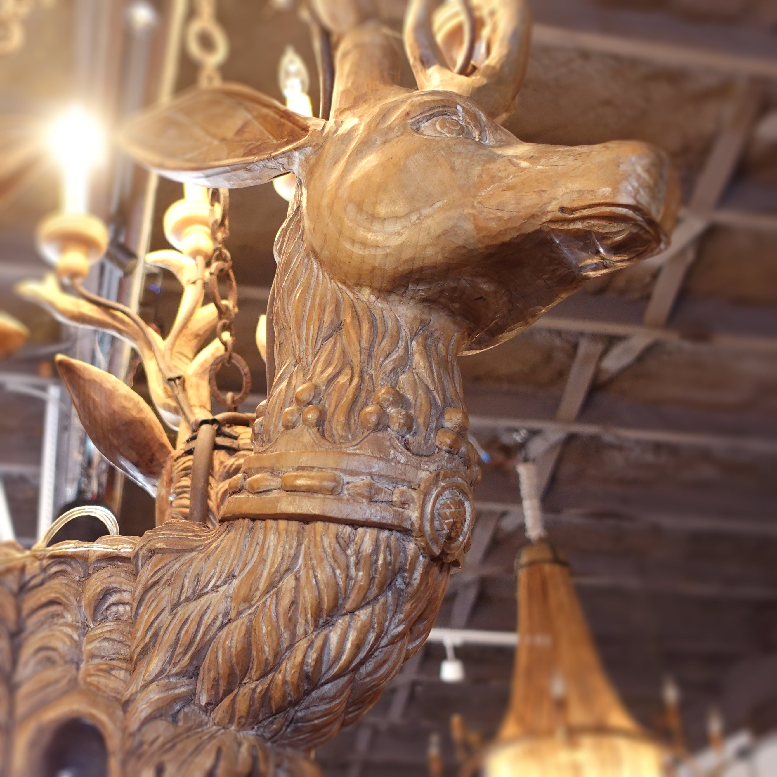 Wooden deer head chandelier with intricate carvings in a warm indoor setting.