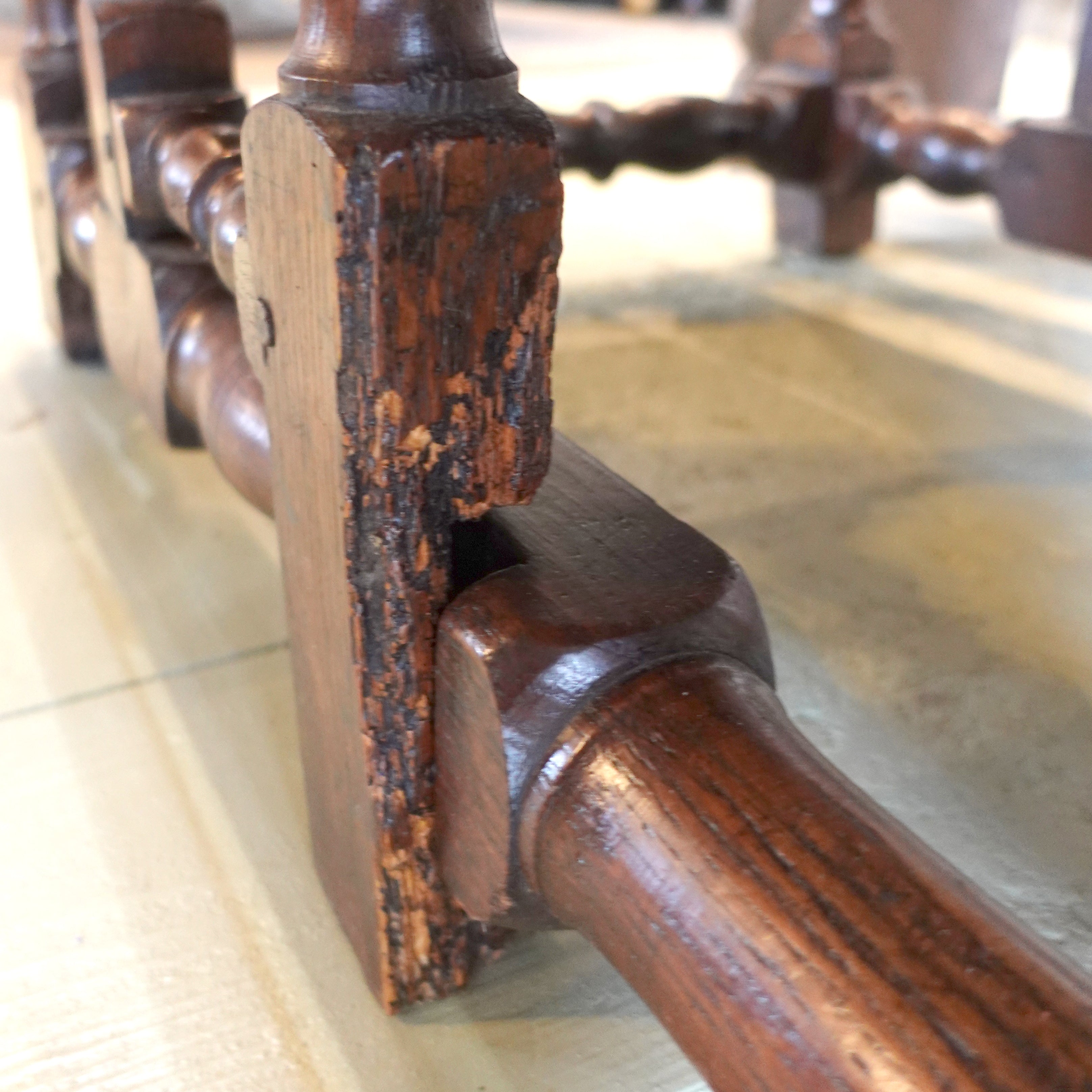 Close-up of a water damage on a wooden leg with a worn finish on a tiled floor.