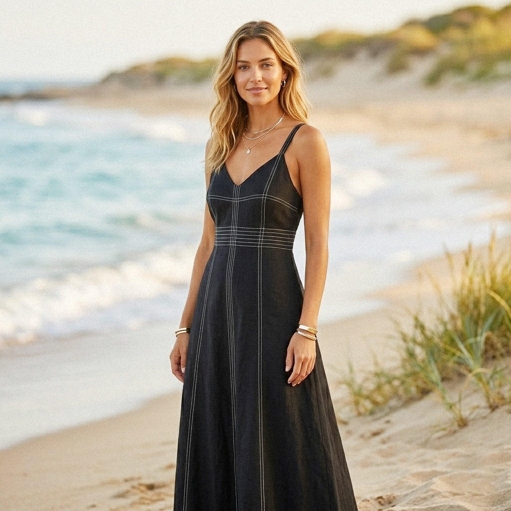 Woman in a black dress standing on a beach with ocean and sand in the background