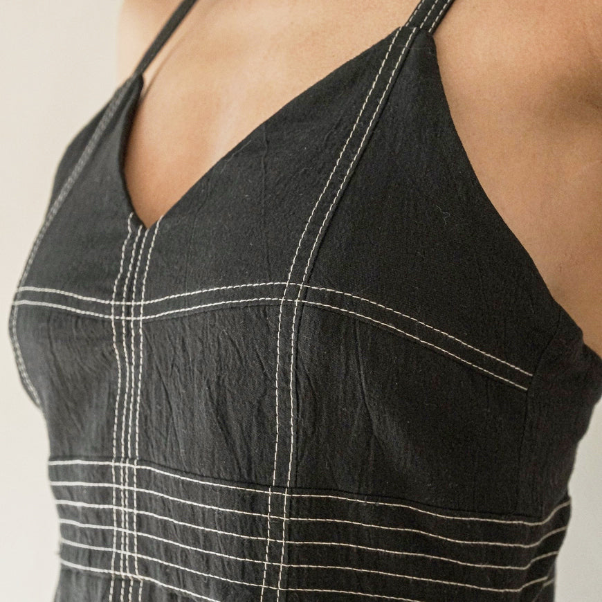 A close-up photograph focusing on the V-neck bodice of the dress, highlighting the fine texture of the black handloom Turkish cotton and the precise detail of the white contrast linear stitching.