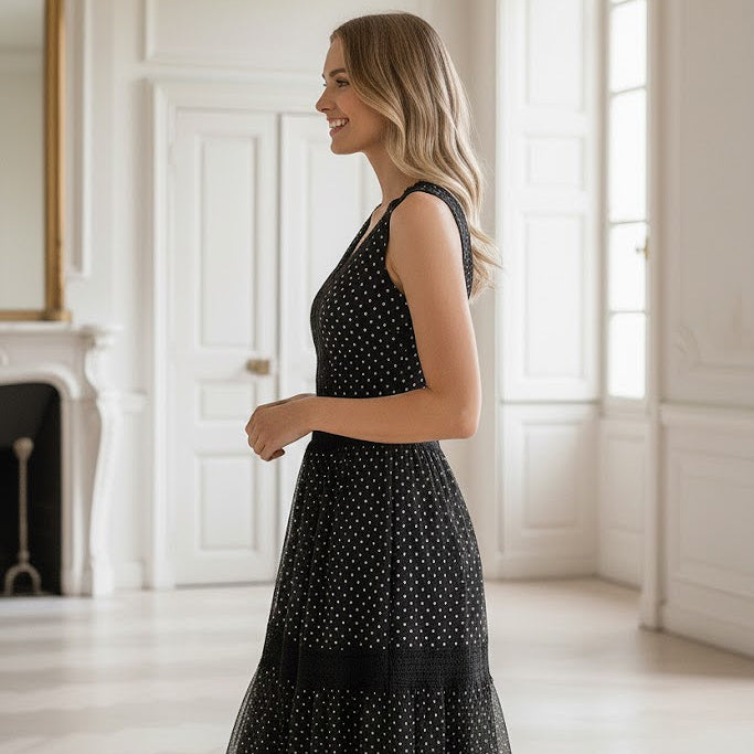 Woman in a black polka dot dress standing in a bright room with white walls and a fireplace.