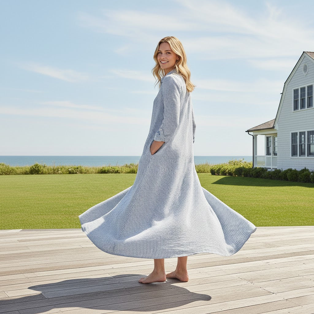 Full-length view of the Meghan navy striped linen dress showing the flowing hemline and side splits in a coastal outdoor setting.