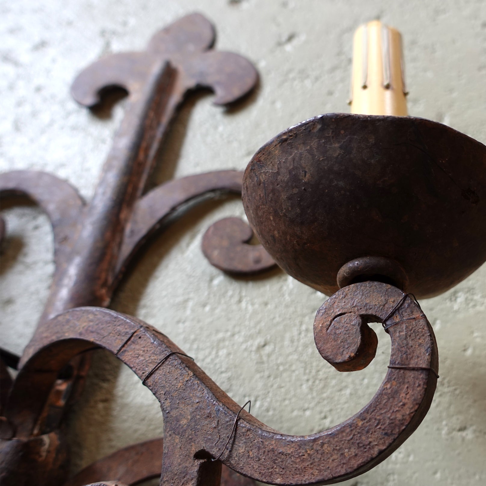 Close-up of a rusted metal candle holder with decorative design on a textured wall.