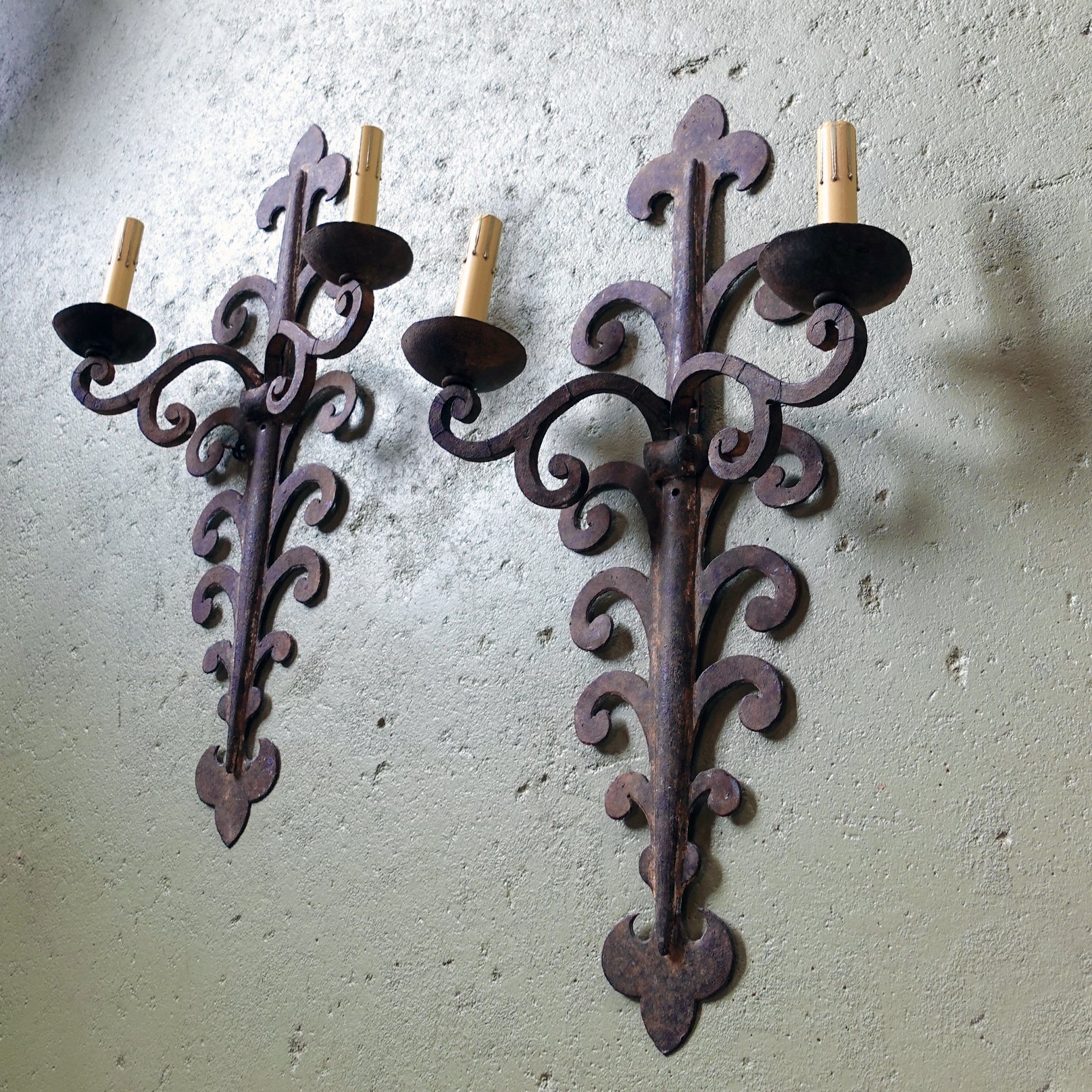 Pair of ornate metal wall sconces on a textured wall.